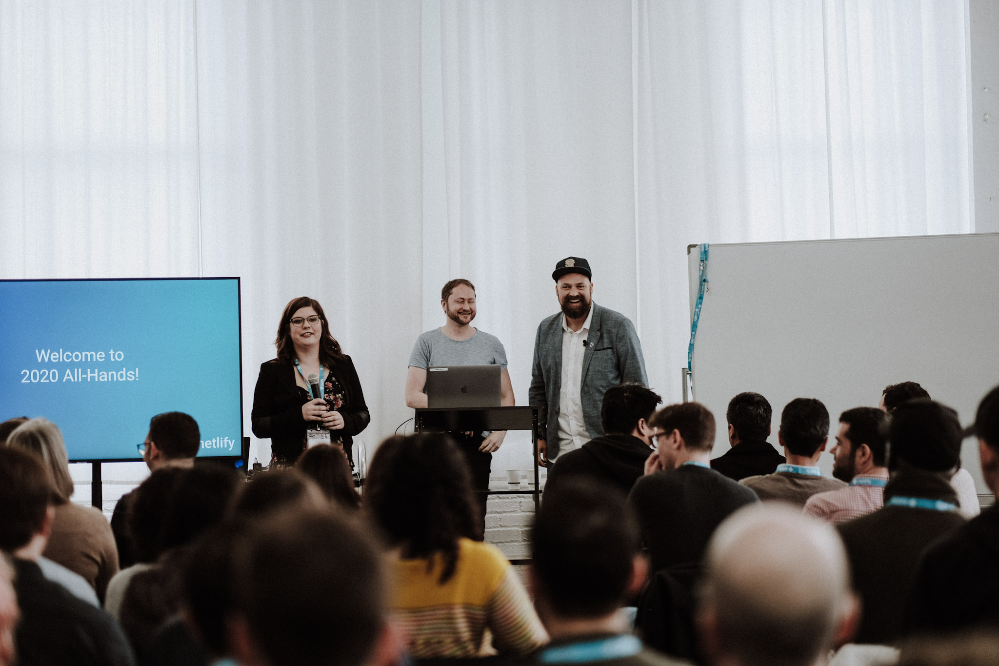 group of people seen sitting facing a stage. on stage are chris and mathias, netlify founders, and madeleine, our office manager.